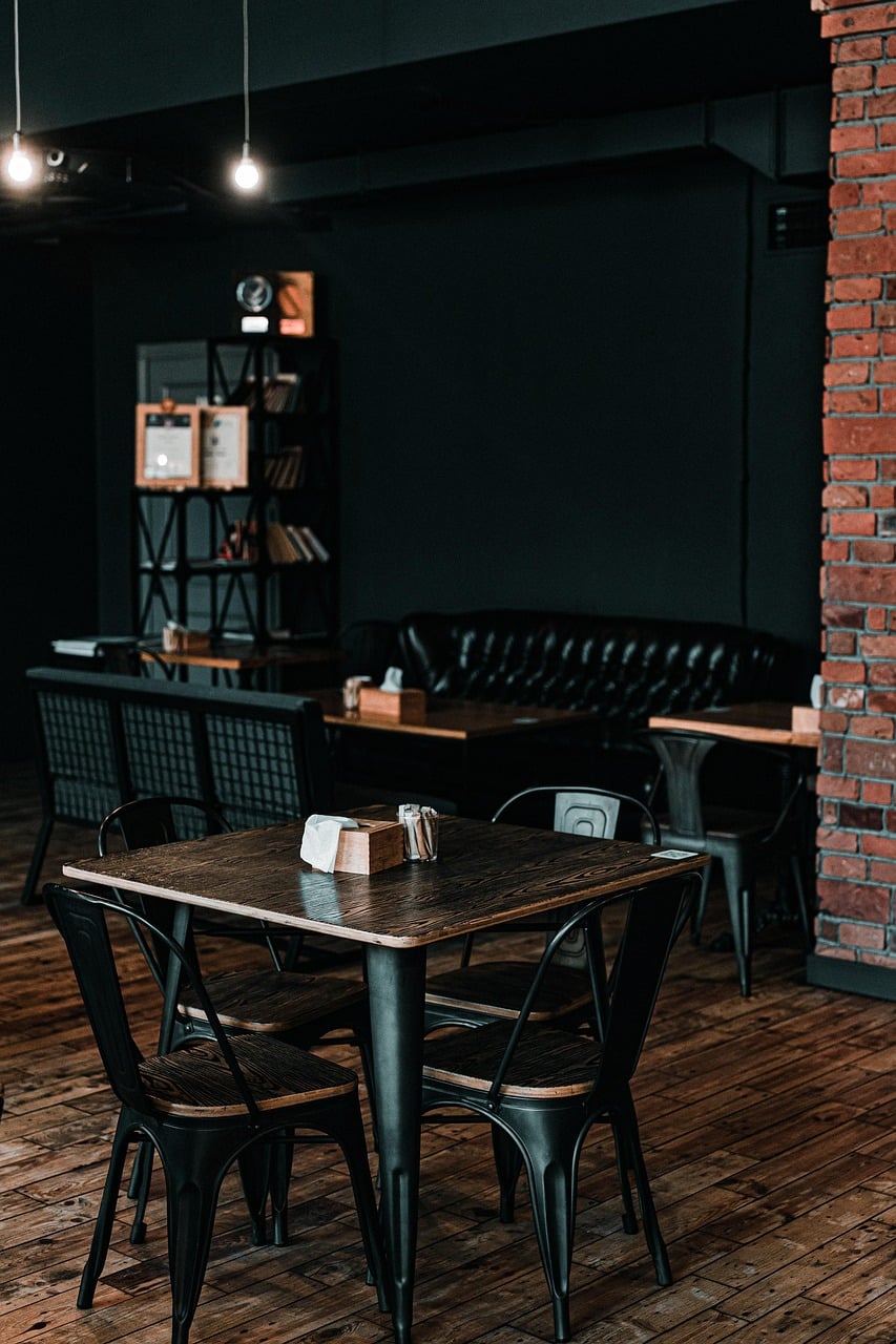 Salle de restaurant dans une ambiance industrielle, murs en briques rouges,  canapé en cuir table en bois et chaises en métal.