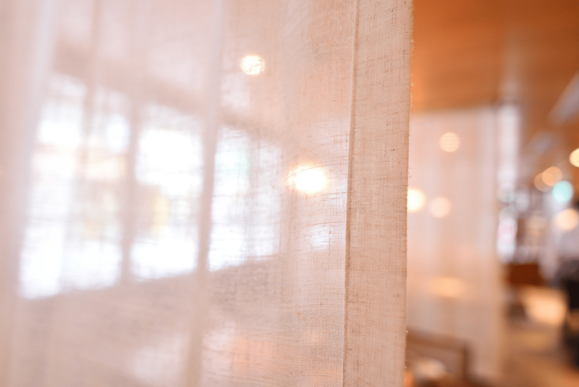 Gros plan sur la texture et la matière d'un voilage en arrière plan on devine une salle de restaurant ou de bar;