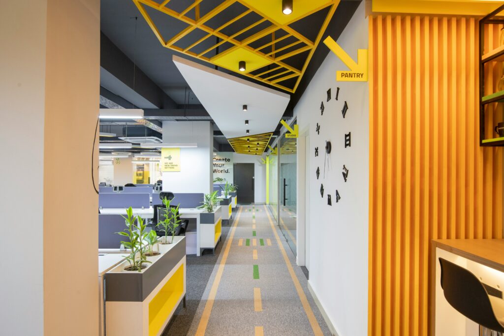 Circulation entre des bureaux ouverts, avec paroi jaune à tasseaux et motifs géométriques au plafond.
